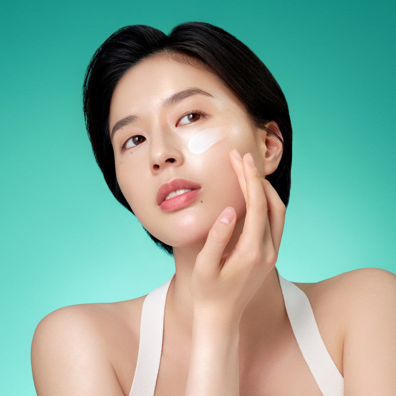 A woman applying Purito bamboo cream for hydration on her cheek, showcasing its smooth texture against a vibrant backdrop