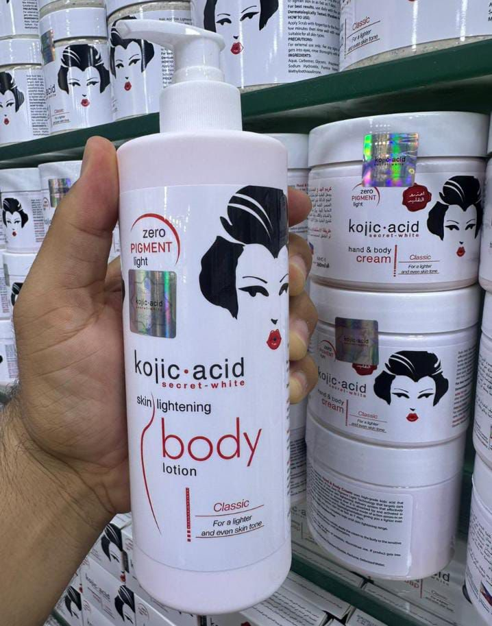 Kojic Acid body lotion held in a hand with shelves of similar products in the background.