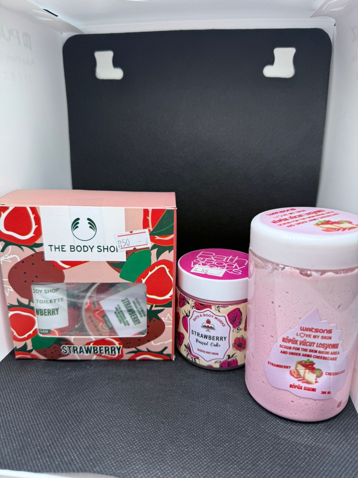 The Body Shop strawberry-themed products including a box, jar, and container on a gray surface.